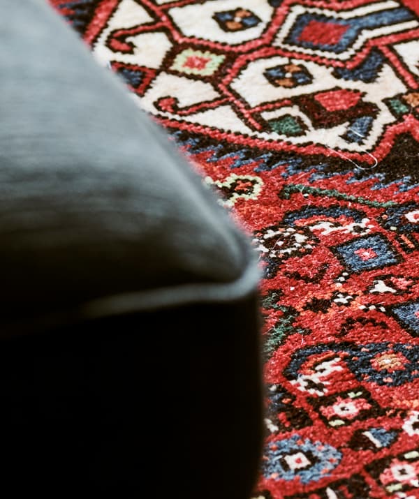Détail d’un tapis d'Orient tissé dans un motif aux formes bleues et vertes sur fond rouge.