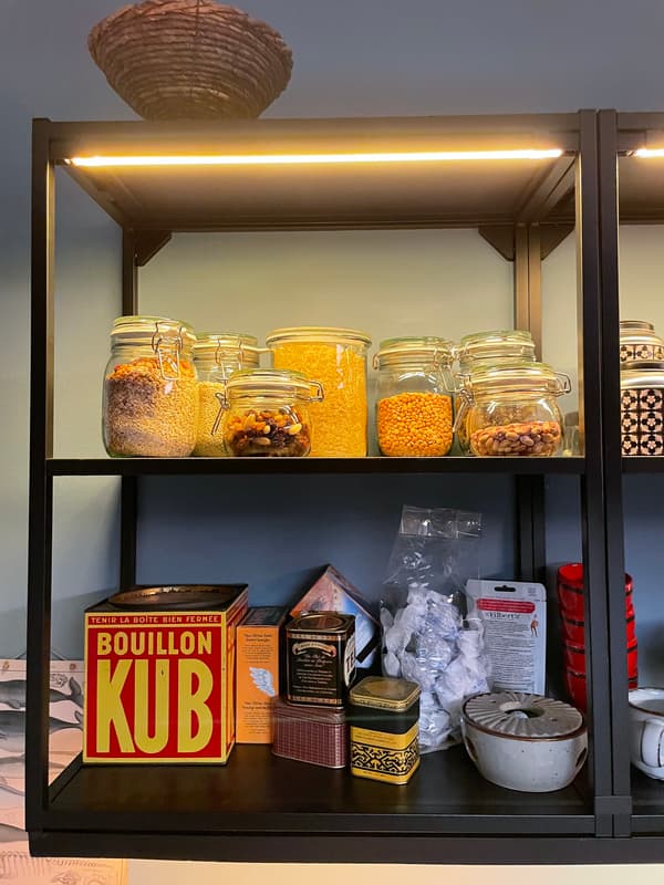 Detail eines offenen Küchenregals mit Beleuchtung in dem Kochzutaten in Gläsern und Dosen stehen. 
