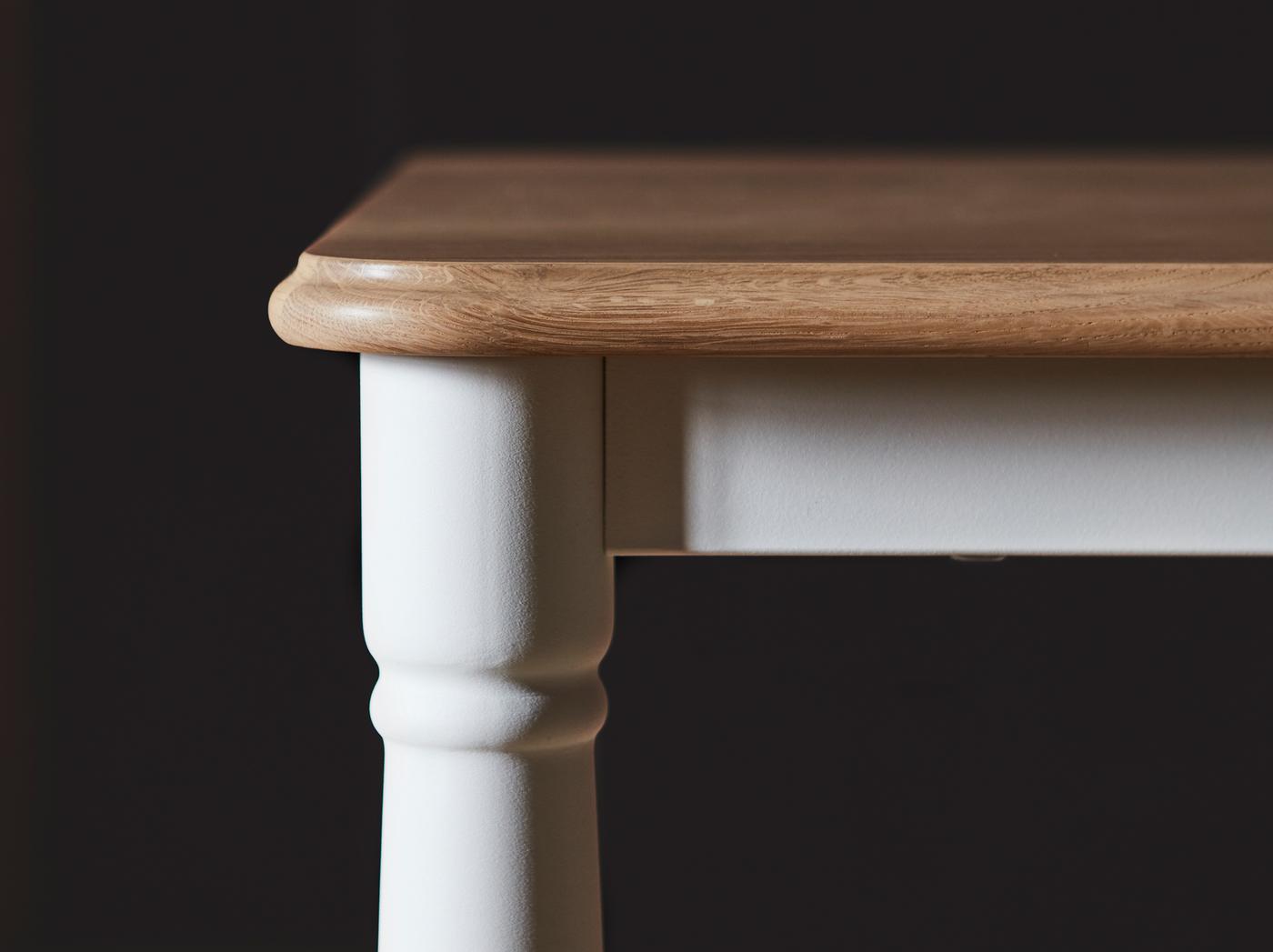 Detail jídelního stolu DANDERYD s deskou stolu z dubové dýhy a bílými nohami ve tvaru v tradičním stylu.