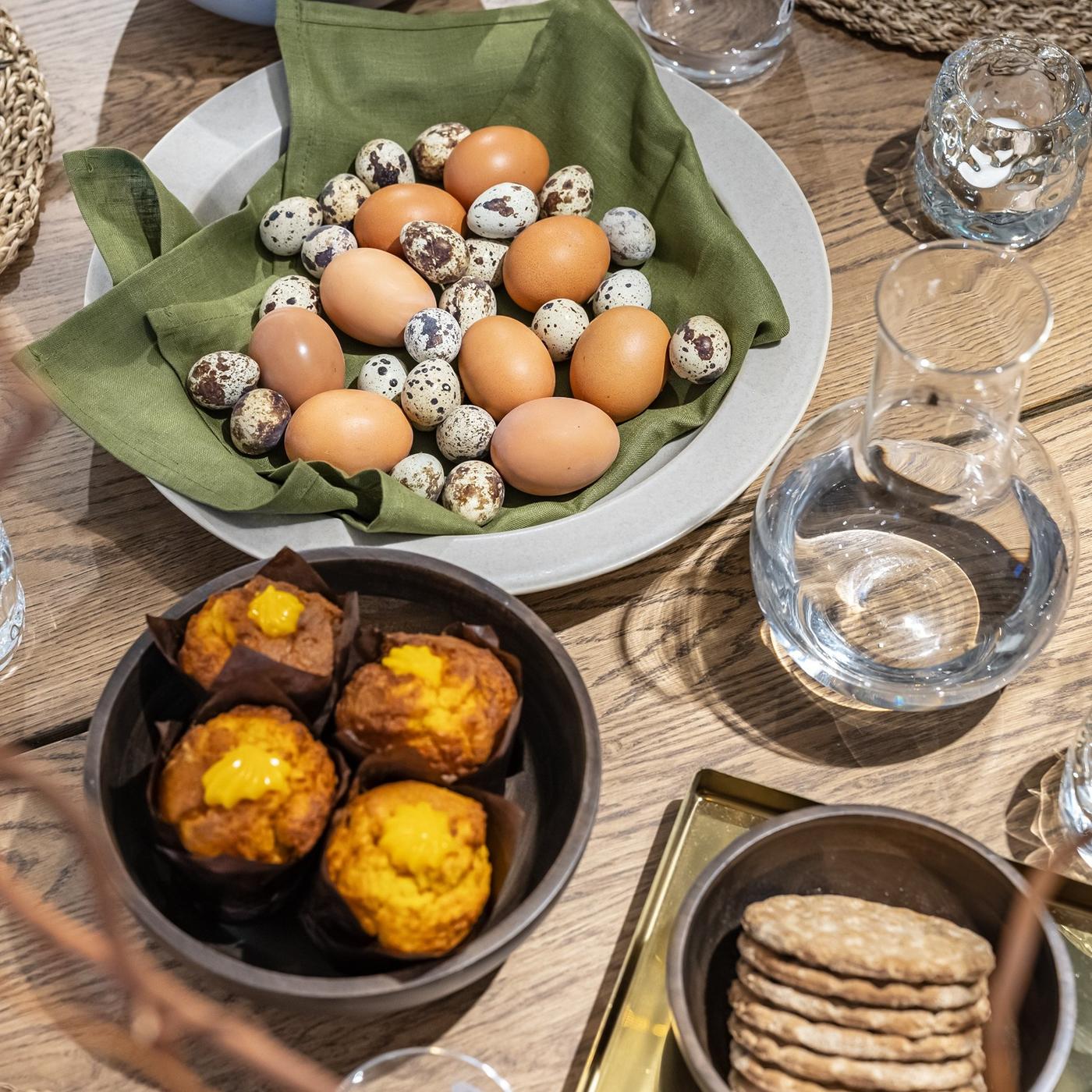 Detail of a festive Easter dining table with natural-toned tableware, cupcakes and neutral-coloured Easter eggs.