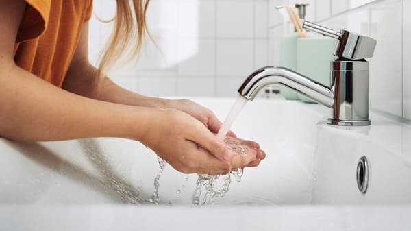 Detail rukou pod vodou tekoucí z vodovodního kohoutku.