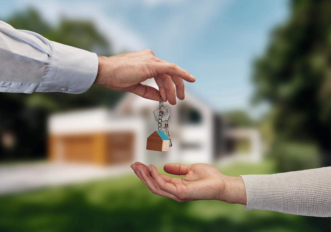 Detail van een hand dat een sleutelhanger in de vorm van een huis in het hand van iemand anders legt.