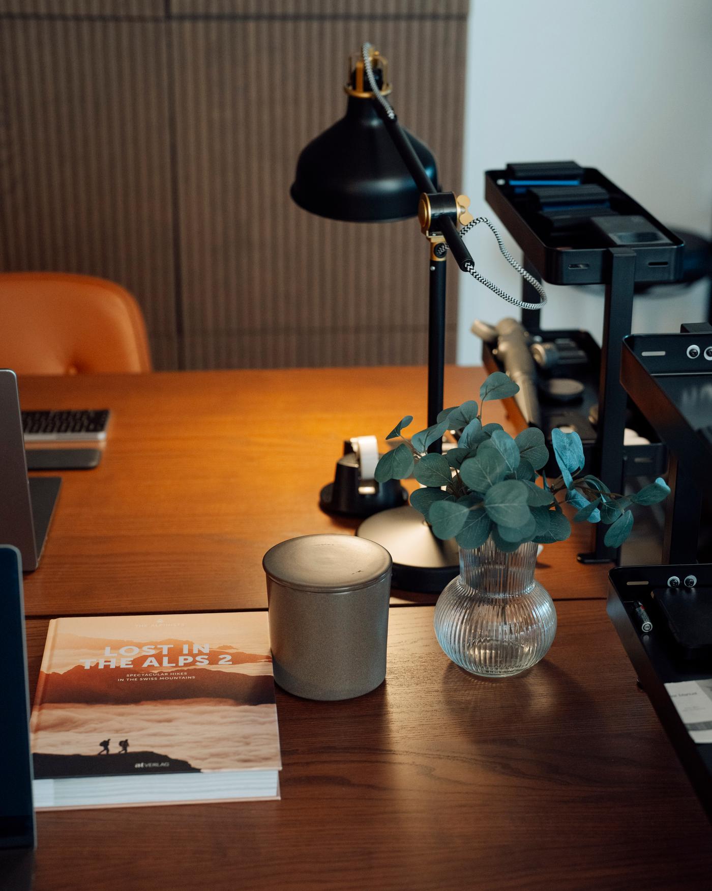 Detailansicht eines Schreibtisch-Arbeitsplatzes mit Schreibtischlampe, Kaffeetasse und einer kleinen Vase. 