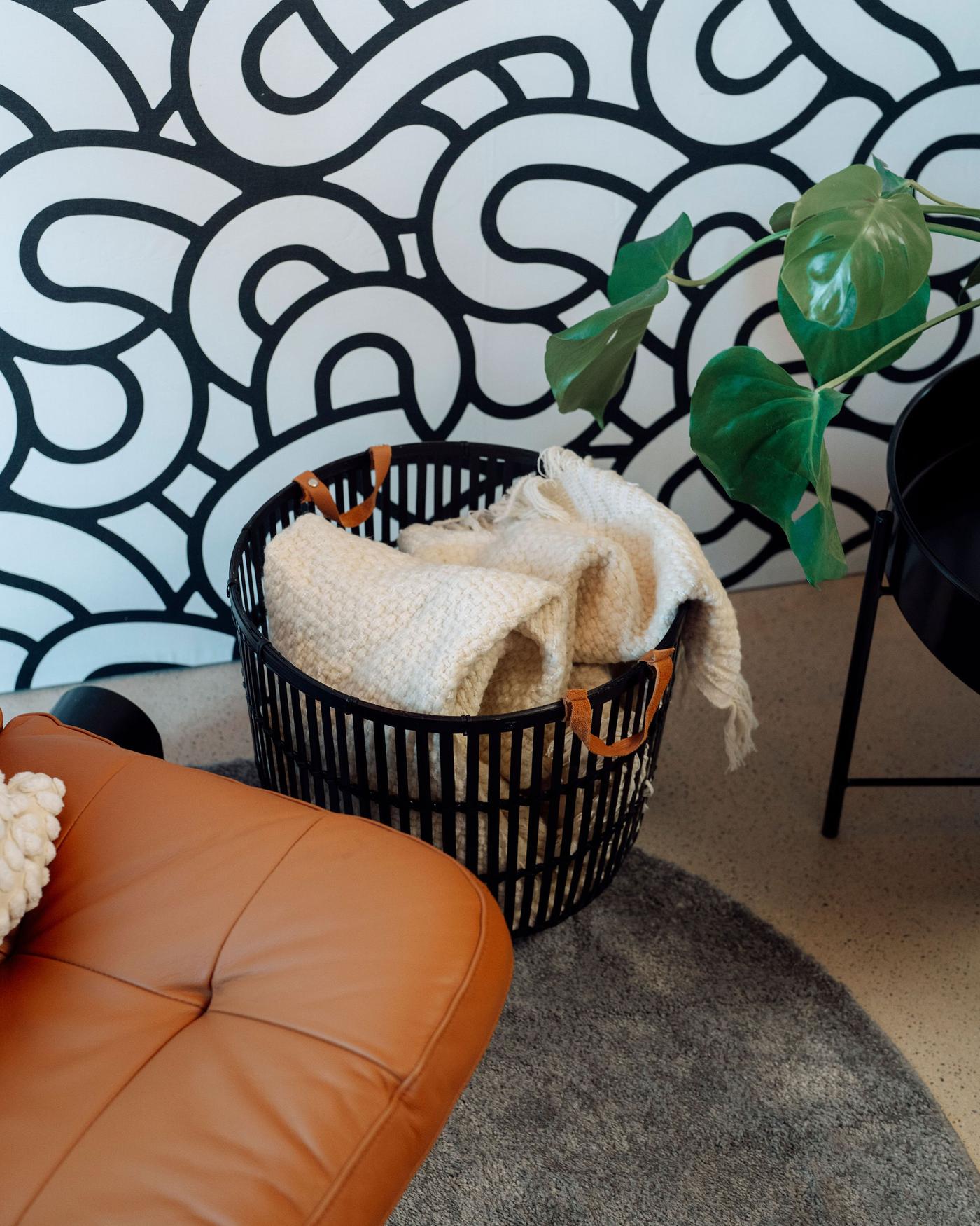 Detailaufnahme eines Korbs neben einem Sessel mit verschiedenen Decken und Plaids darin. 