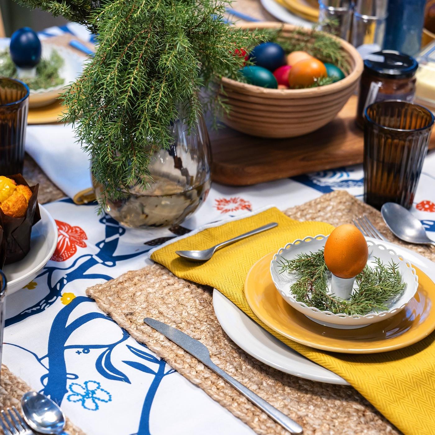 Detailed table setting with blue and yellow accents, including a decorative egg served on a candlestick used as an egg cup.
