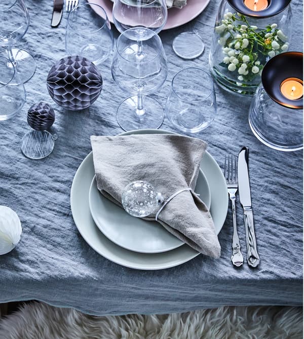 Detalle da mesa con vaixela en cores pastel, pezas de cristalería e panos de mesa de liño decorados con bólas de cristal.