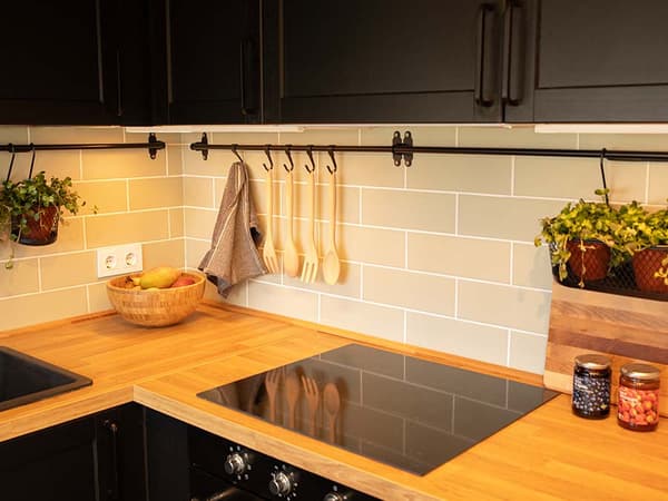 Detalle de encimera con vitrocerámica, plantas, cestas, paño de cocina, barra con colaganes.