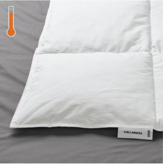 Detalle de una cama, se muestra en primer plano un edredón FJÄLLARNIKA y en la esquina superior izquierda un termométro ''cálido''''.