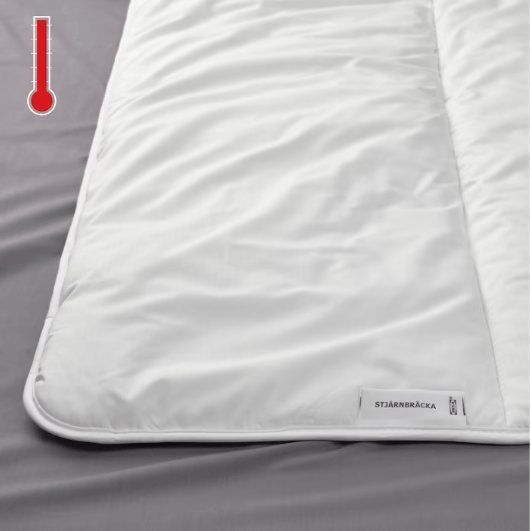 Detalle de una cama, se muestra en primer plano un edredón STJÄRNBRÄCKA y en la esquina superior izquierda un termométro ''caliente''.