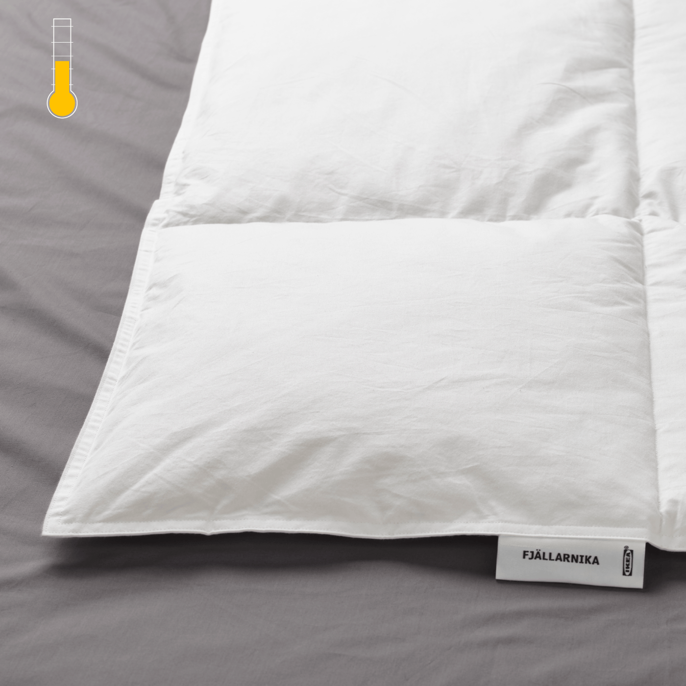 Detalle de una cama, se muestra en primer plano un plumón FJÄLLARNIKA y en la esquina superior izquierda un termométro ''cálido''''.