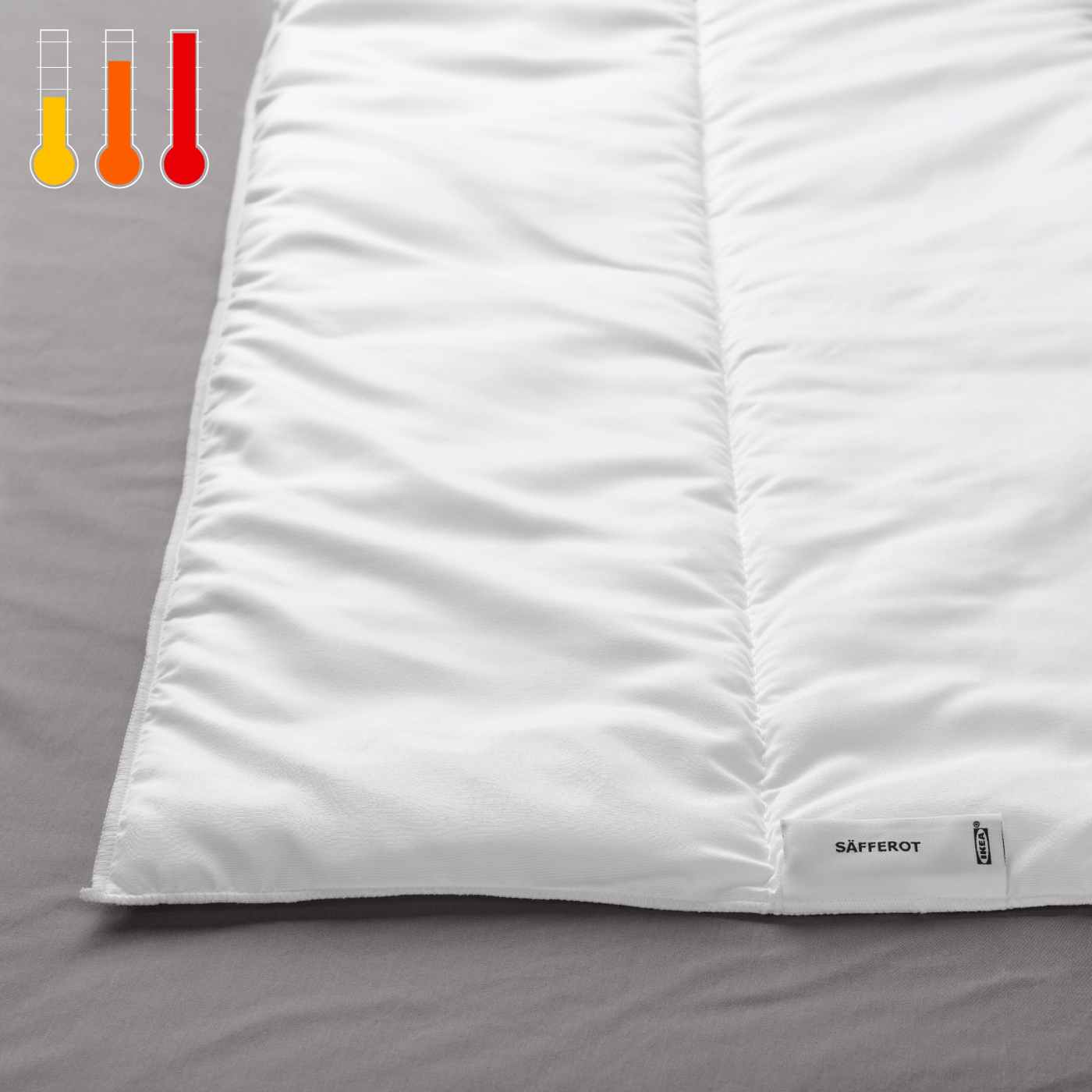 Detalle de una cama, se muestra en primer plano un plumón SÄFFEROT y en la esquina superior izquierda un termométro ''tibio''.'.