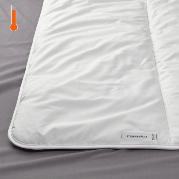 Detalle de una cama, se muestra en primer plano un plumón STJÄRNBRÄCKA y en la esquina superior izquierda un termométro ''caliente''.