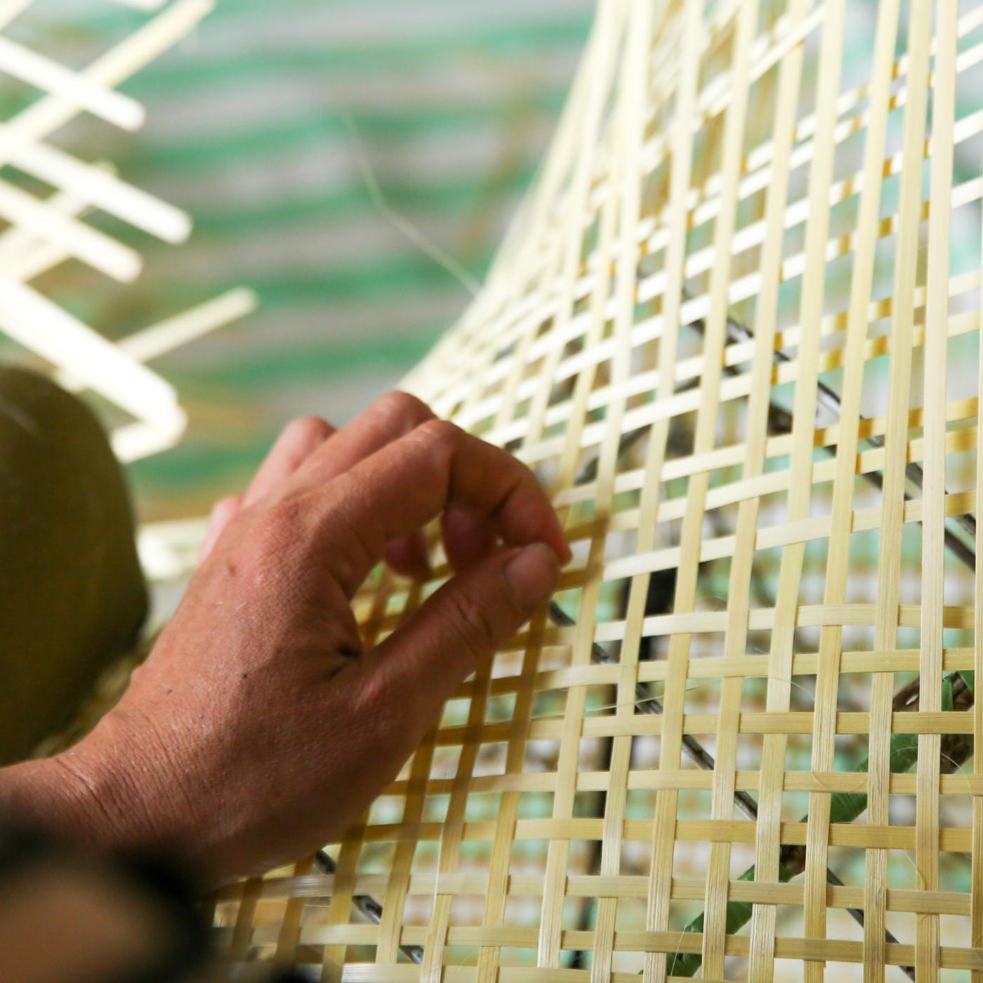 Detalle de una mano tejiendo una silla de ratán.