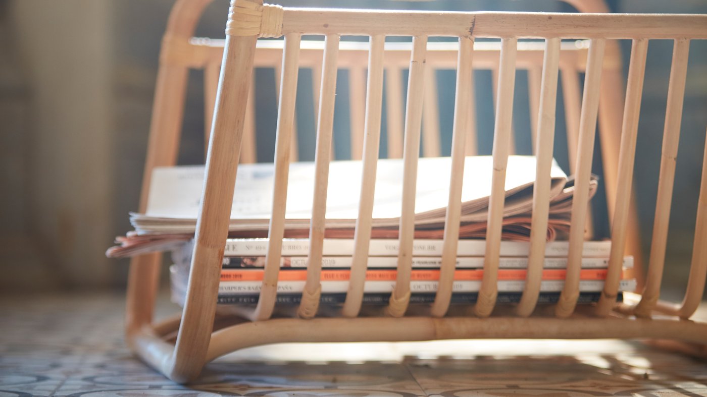 Detalle del soporte de revistas BUSKBO hecho a mano en ratán, donde se guardan algunas revistas, colocado en el suelo.