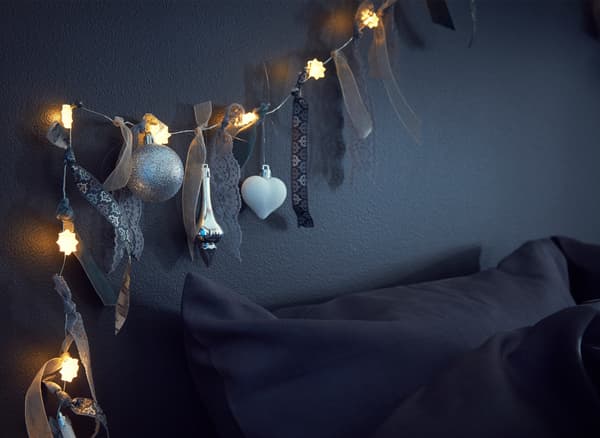Detalle dunha grilanda luminosa decorada con fitas, tiras de tea e adornos sobre unha cama.