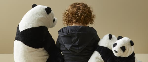 Dete sedi na podu okruženo plišanim panda igračkama