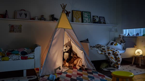Dětský stan HÖVLIG s barevným kobercem BUSENKEL a plyšovými hračkami uvnitř, mezi dvěma různými bílými prodloužitelnými postelemi.