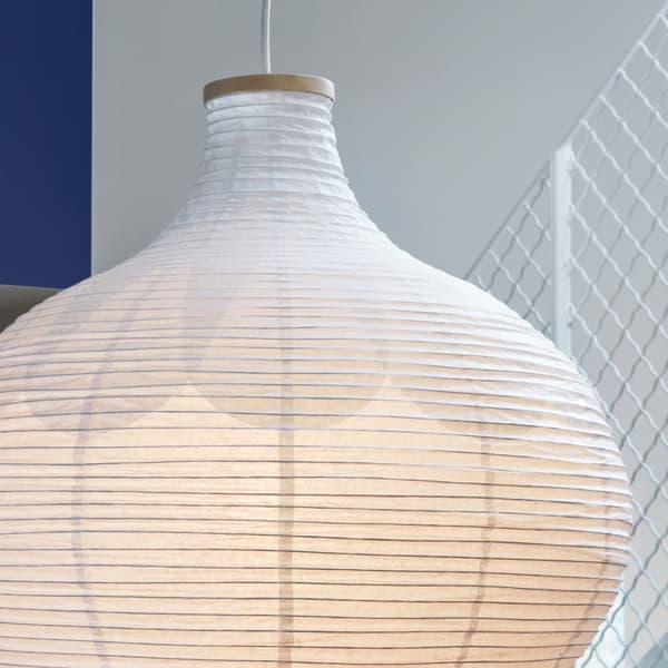 Dettaglio del paralume per lampada a sospensione RISBYN, la cui forma ricorda quella di una cipolla, realizzato in carta di riso e caratterizzato da un motivo delicato. Sullo sfondo una scala. - IKEA