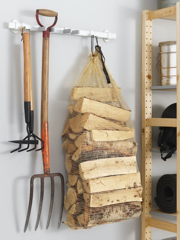 Dettaglio di un garage in cui sono appesi a dei ganci alcuni oggetti da lavoro come un forcone e una vanga. C'è anche una rete con all'interno della legna.