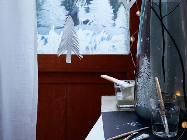 Dettaglio di un vaso con decorazioni natalizie, pennelli e una finestra decorata.