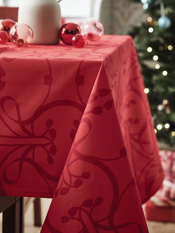 Dettaglio di una tovaglia rossa natalizia con decorazione. Sopra, ci sono delle palline di Natale e sullo sfondo un labero.