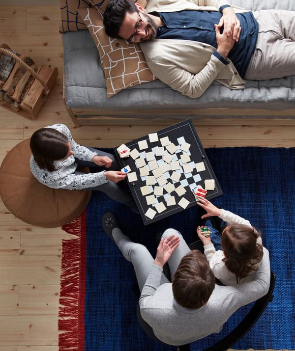 Deux adultes et deux enfants assis ou couchés autour d’un jeu de société posé sur une table basse.