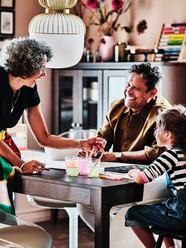 Deux adultes et un enfant autour d’une table extensible EKEDALEN en brun foncé. L’enfant est assis sur une chaise junior AGAM en noir.