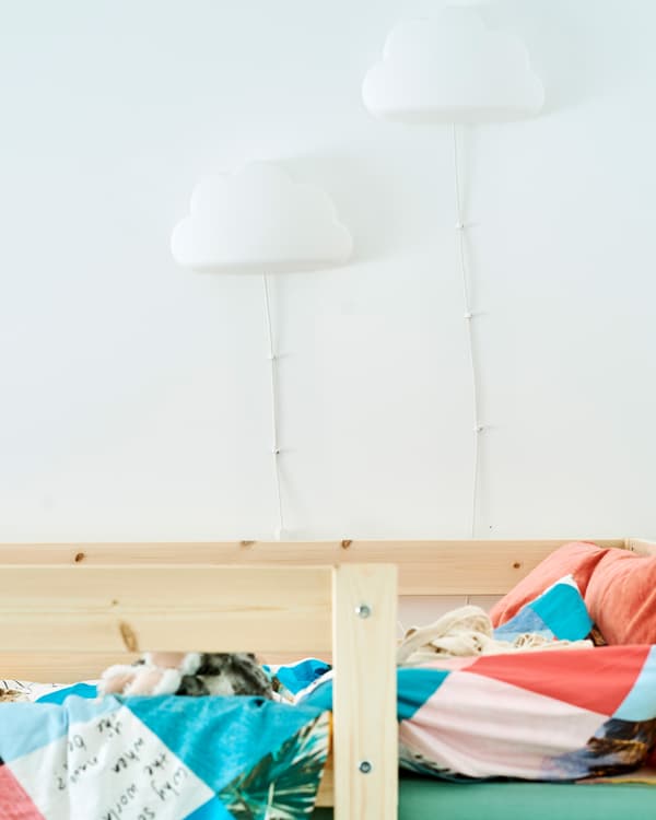 Deux appliques en forme de nuage fixées au mur au-dessus d’un cadre de lit en bois; le lit est revêtu de linge de lit coloré.