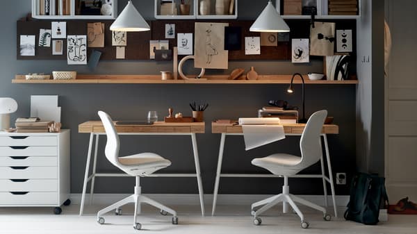 Deux bureaux LILLÅSEN contre un mur, chaises de bureau et caisson à tiroirs blanc, étagères, tableaux d'affichage et deux suspensions blanches.