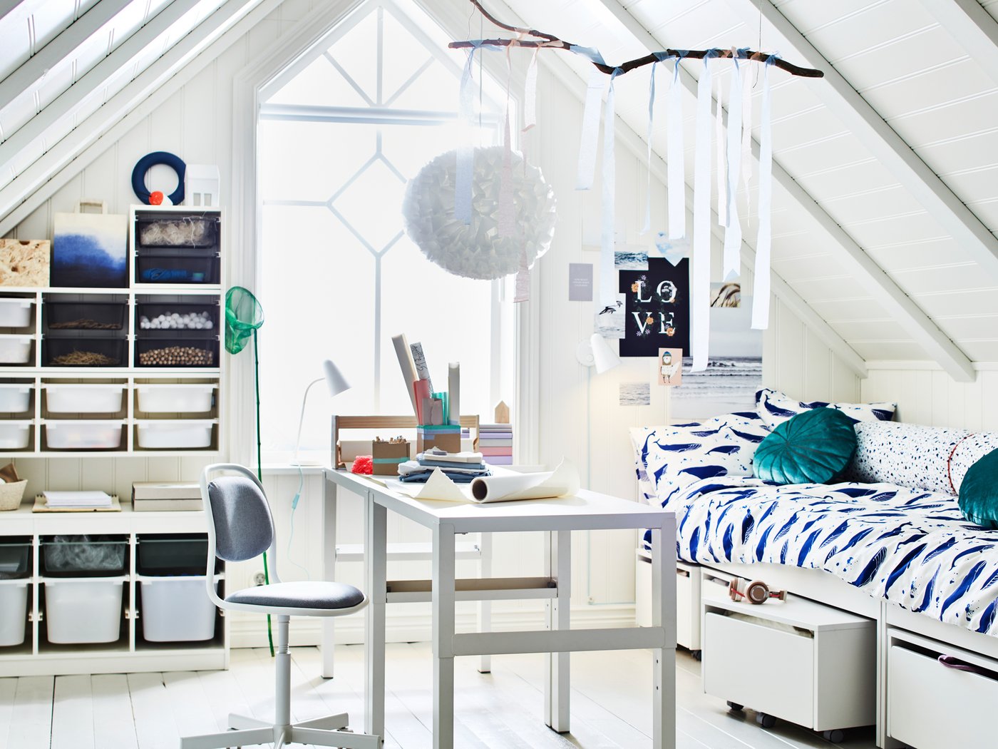 Deux bureaux PÅHL sont installés au milieu d’une pièce avec plafond incliné et haute fenêtre, près d’un lit et de rangements TROFAST.