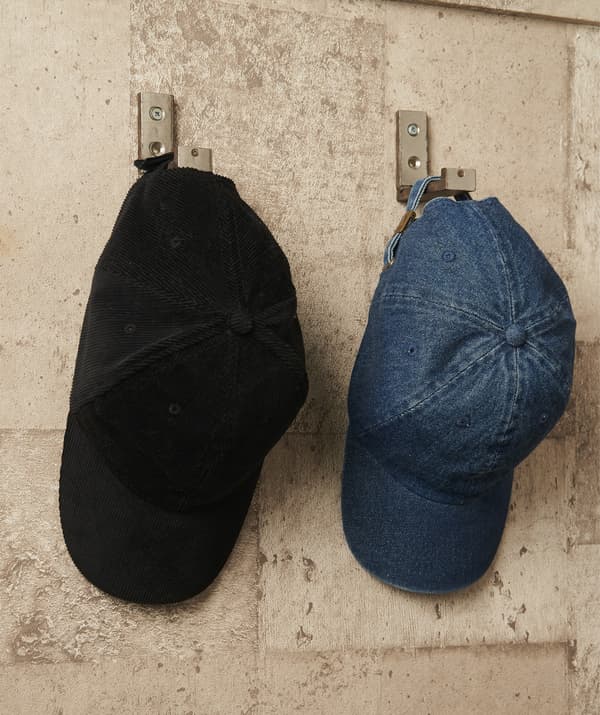 Deux casquettes pendues à des crochets argentés fixés à un mur en briques.