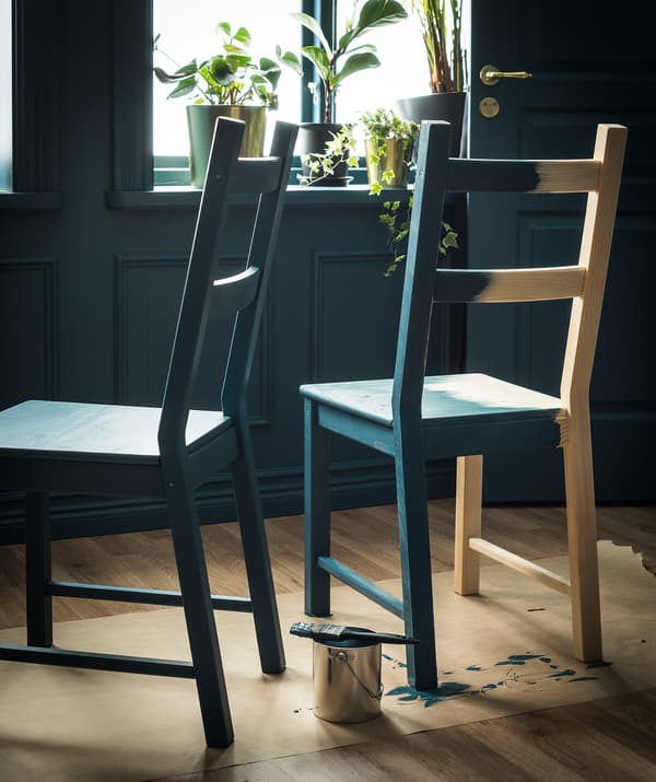 Deux chaises en bois blond sur un papier de protection pour plancher. Les chaises en bois non traité sont peintes avec une couleur foncée.