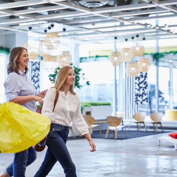 Deux clientes IKEA qui se baladent dans le magasin avec un sac jaune à la main.