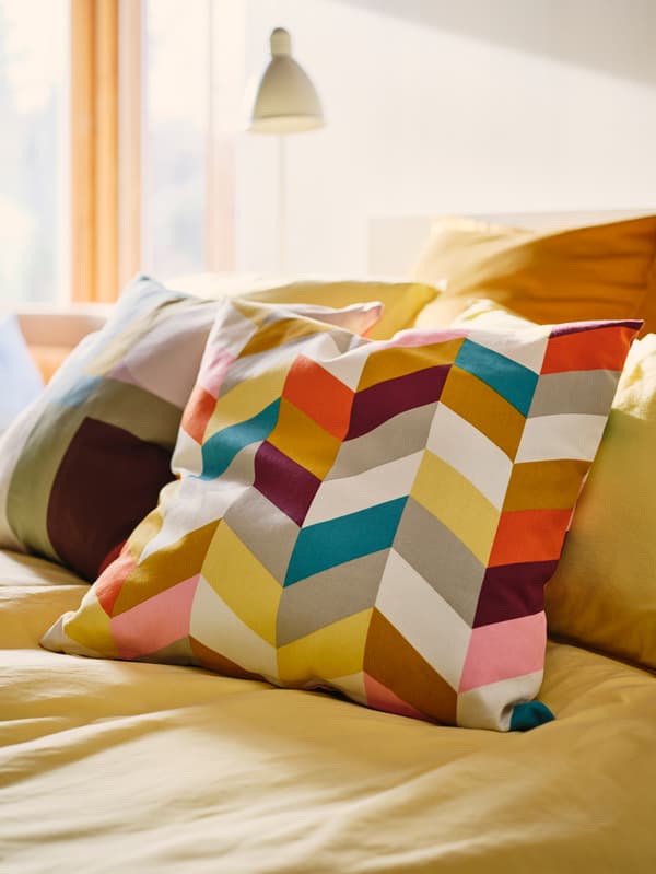 Deux coussins, recouverts des housses HANNELISE et STENMÄTARE, sur une housse de couette jaune vif dans une chambre à coucher.