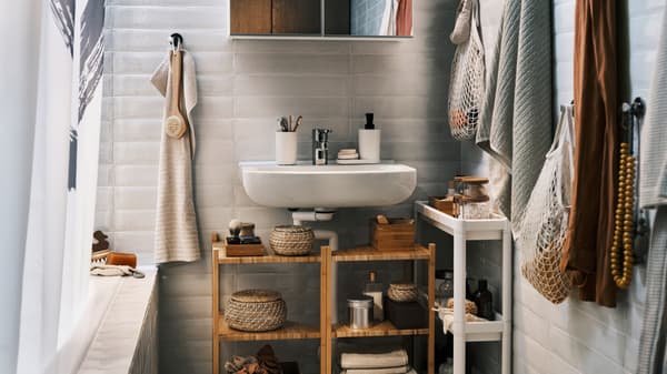 Deux étagères d’angle en bambou sous un lavabo blanc avec un meuble à miroir au-dessus, plus un chariot et une serviette.