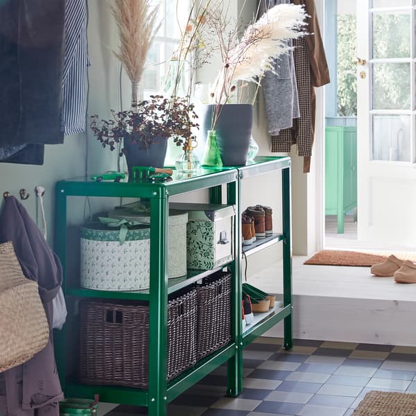 Deux étagères KOLBJÖRN en vert dans un hall d’entrée. Des boîtes et des corbeilles sont posées sur les tablettes, et des plantes vertes sur le plateau supérieur.