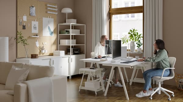 Deux femmes dans un espace de travail aménagé dans le salon, assises sur des chaises pivotantes devant deux bureaux se faisant face.