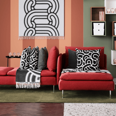 Deux méridiennes rouge en tissu avec des coussins de décoration aux motifs abstraits noir et blanc.