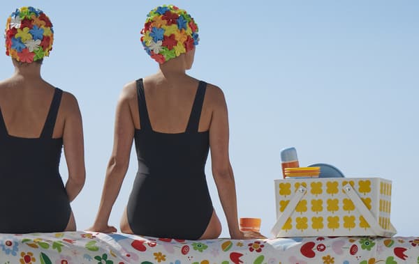 Deux nageuses assises sur un tissu à motifs à côté d’un panier à pique-nique.