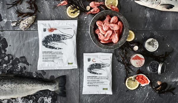 Deux paquets IKEA SJÖRAPPORT avec des crevettes congelées en deux tailles, entourées de décorations alimentaires sur une ardoise noire.