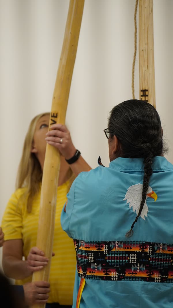 Deux personnes aident à construire un tipi et tiennent un grand morceau de bois. 