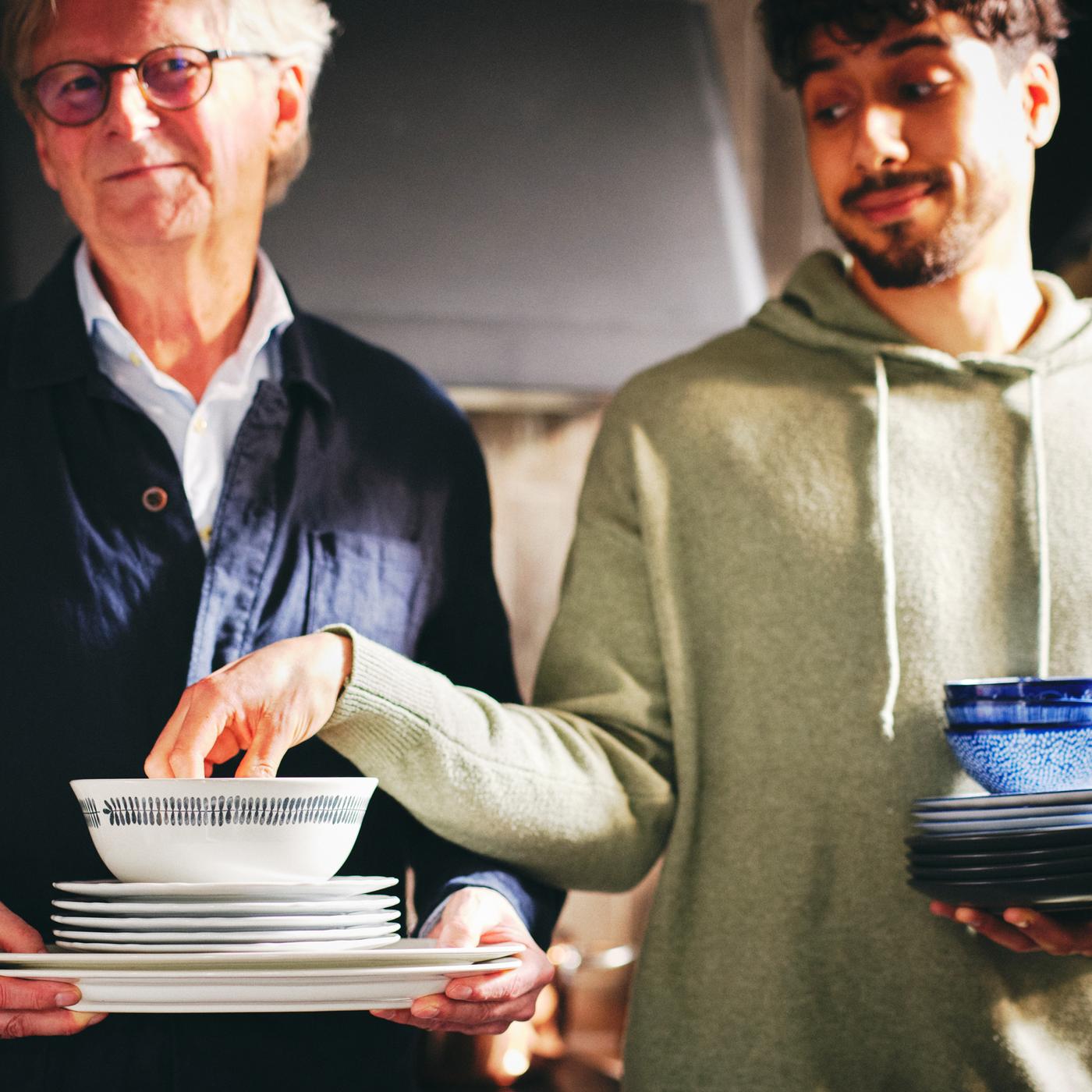Deux personnes, dont une qui tient une pile d’assiettes à salade et de plats UPPLAGA blancs ainsi qu’un bol FRIKOSTIG blanc à motifs.