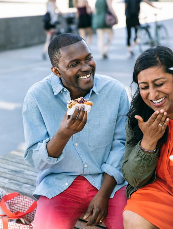 Deux personnes en train de sourire et de manger un hot-dog végétarien.