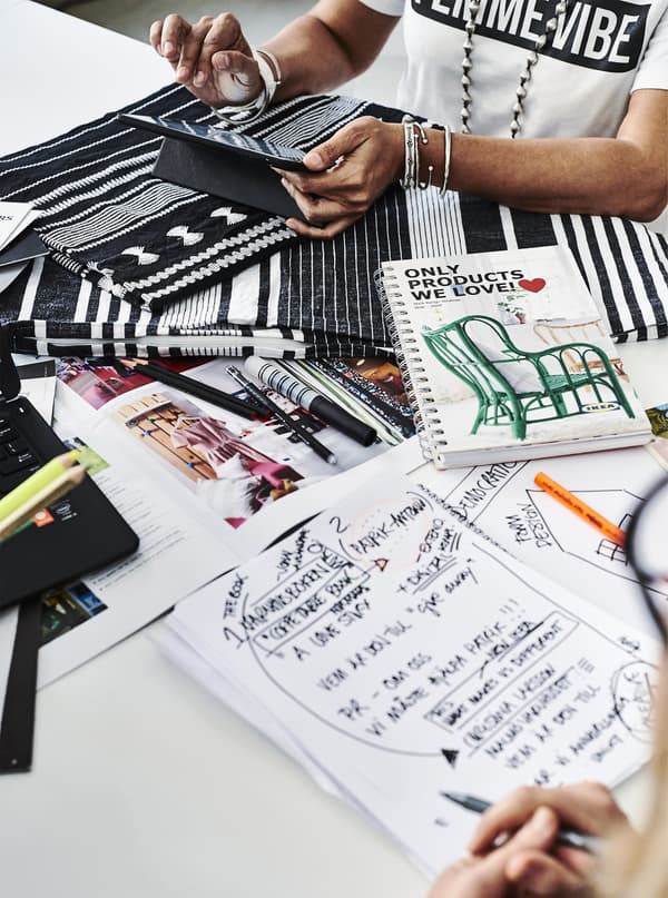 Deux personnes en train de travailler avec du tissu et des carnets sur un bureau.