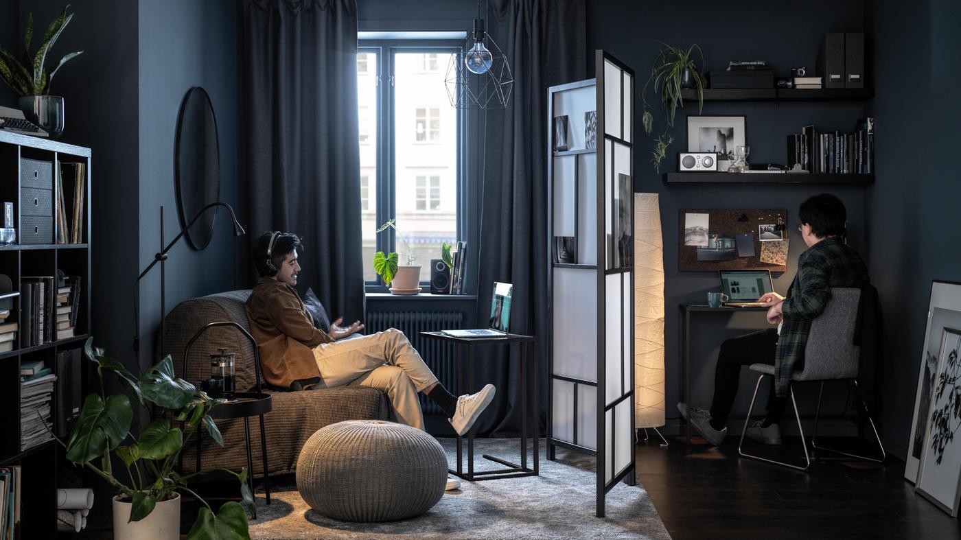 Deux personnes installées dans deux parties d’un séjour séparées par un paravent RISÖR, toutes deux regardant leur écran.