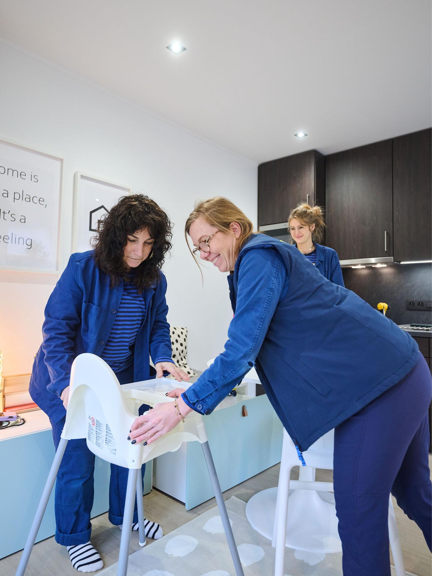 Deux personnes installent une chaise haute dans une cuisine moderne aux armoires foncées et murs clairs.