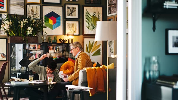 Deux personnes jouent aux cartes autour d’une table basse KRAGSTA placée devant un mur galerie décoré d’un assortiment d’affiches BILD encadrées.