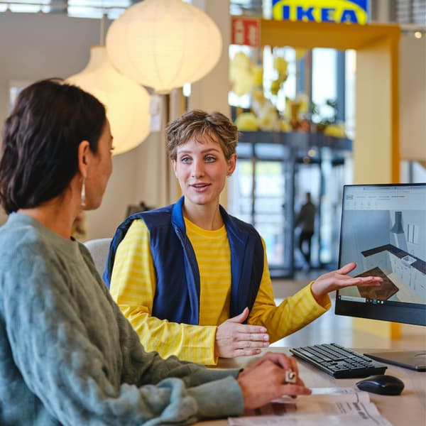 Deux personnes sont assises à un bureau dans un magasin IKEA et regardent un écran d'ordinateur.