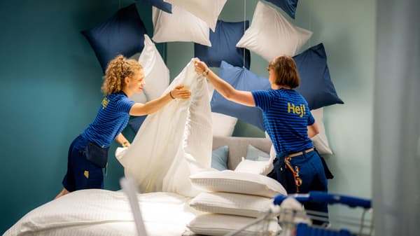 Deux personnes vêtues de chemises IKEA bleues disposent de grands coussins moelleux et de la literie dans un showroom très cool.