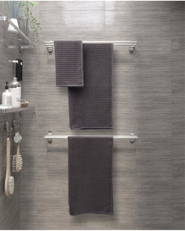 Deux porte-serviettes en acier inoxydable sont installés au mur, l’un au-dessus de l’autre. À proximité, on voit deux étagères en verre portant des articles d’hygiène.